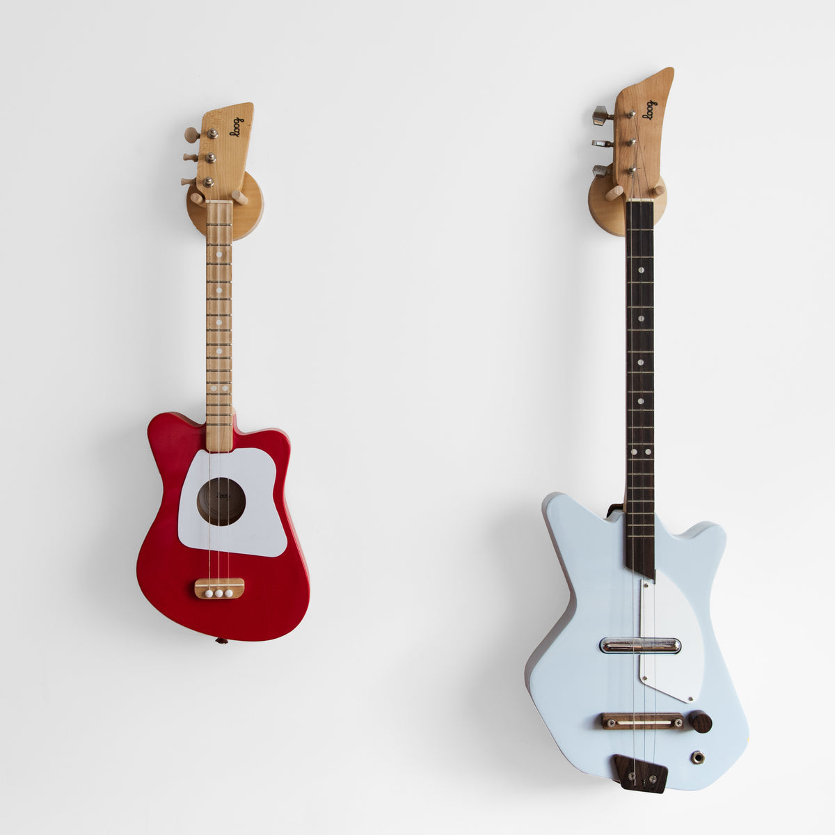 Red and light blue Loog guitars displayed on wooden wall hangers.