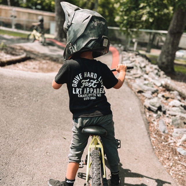 Child on bike wearing black APEX LIVE FAST TEE with helmet.