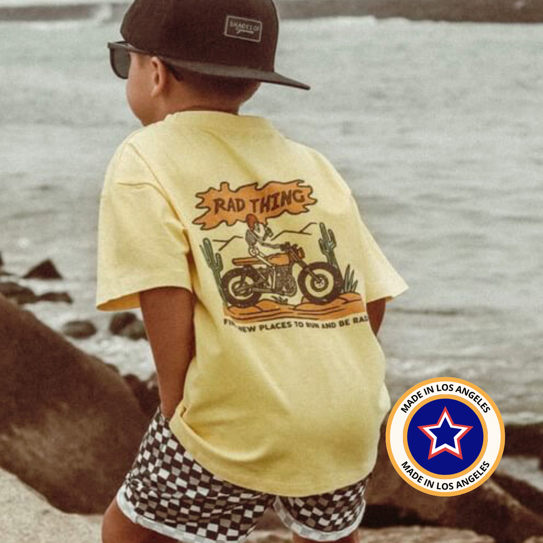 Boy wears Golden Yellow 'Where the Rad Things Are' tee with motorcycle graphic at beach.