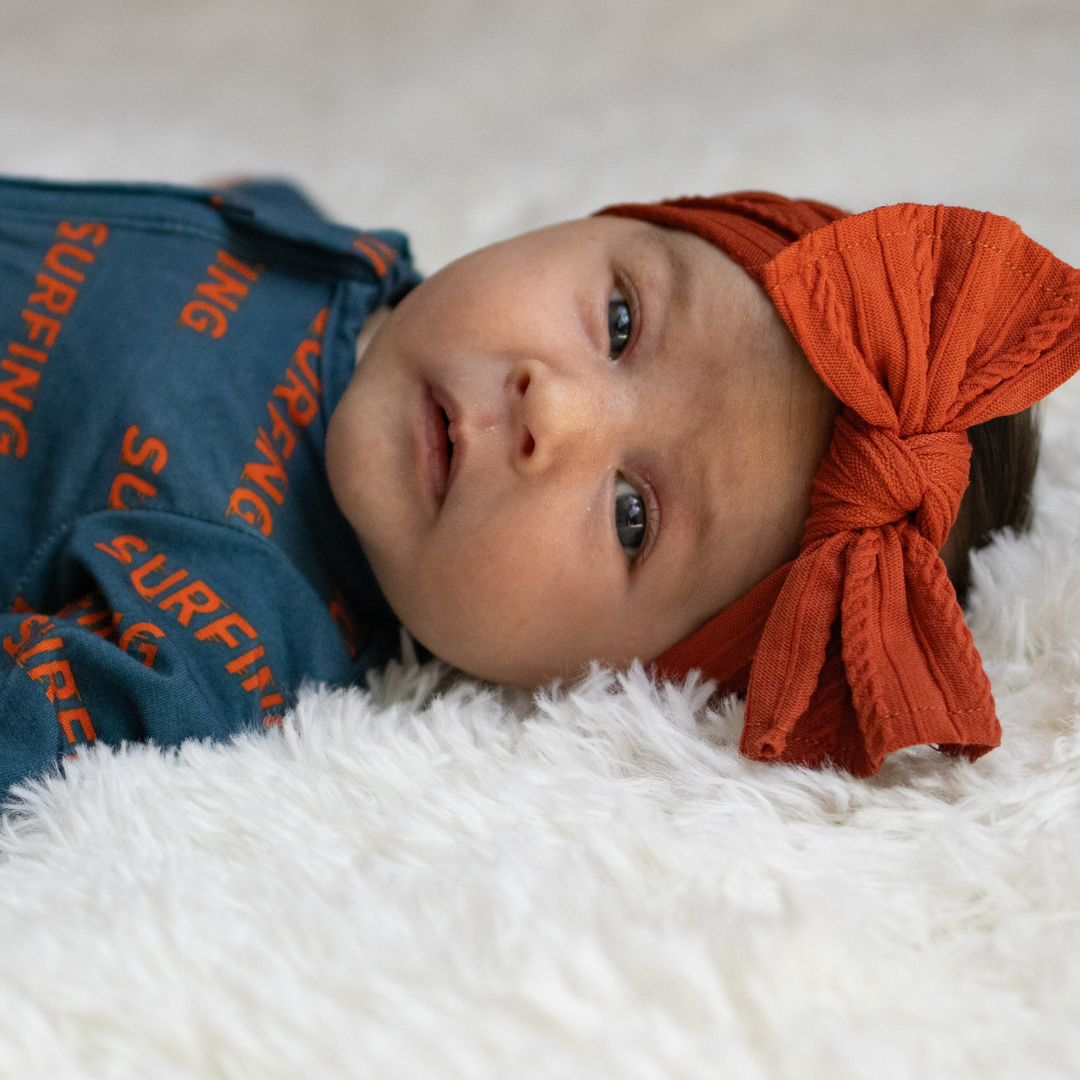 Baby in Ocean Cubs Wear Pipeline Dreams bamboo sleeper with orange headband.