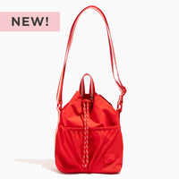 NEW! Cherry Motion Bucket Crossbody bag in bright red with a drawstring closure and white striped strap.