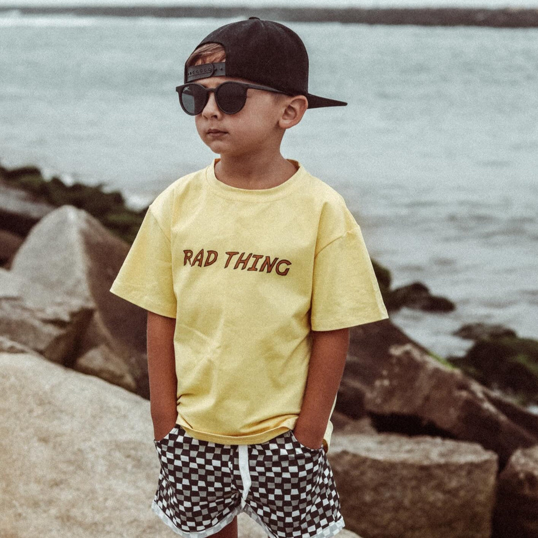 Toddler in Golden Yellow 'Where the Rad Things Are' tee and checkerboard shorts.