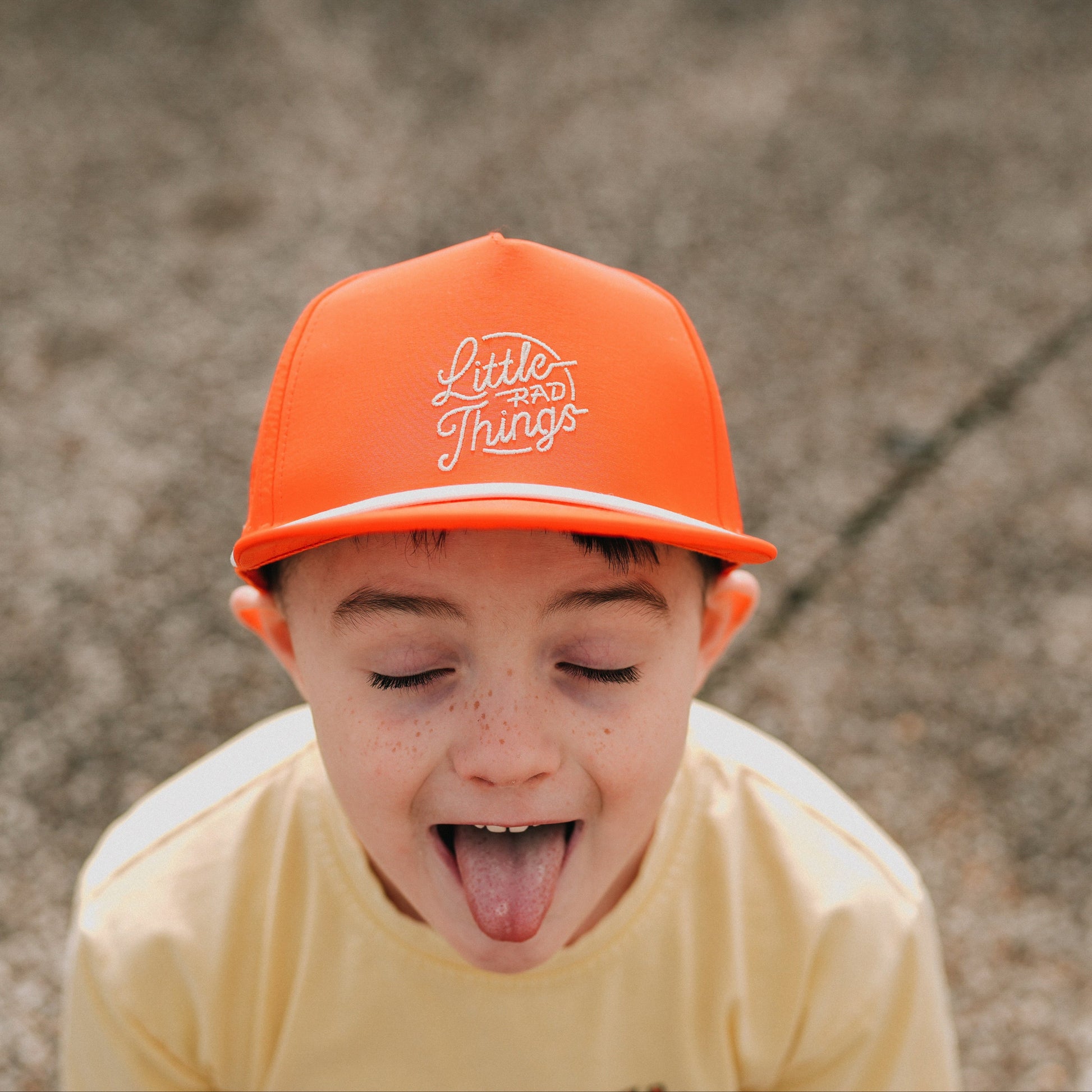 Boy wearing orange 'Little Rad Things' hat, sticking out tongue.