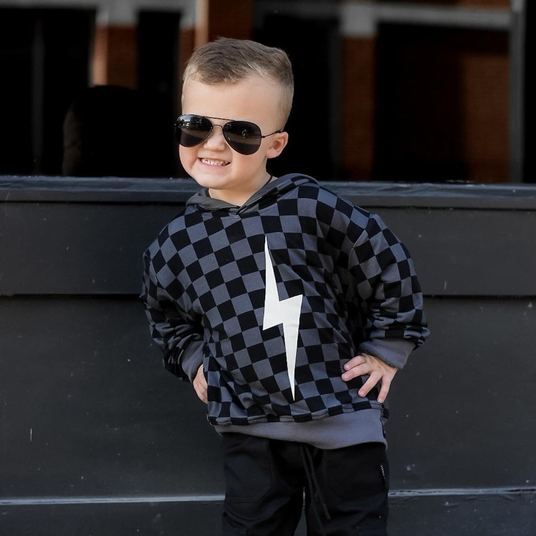 Boy smiles in black checkered Spark Hoodie with lightning bolt.