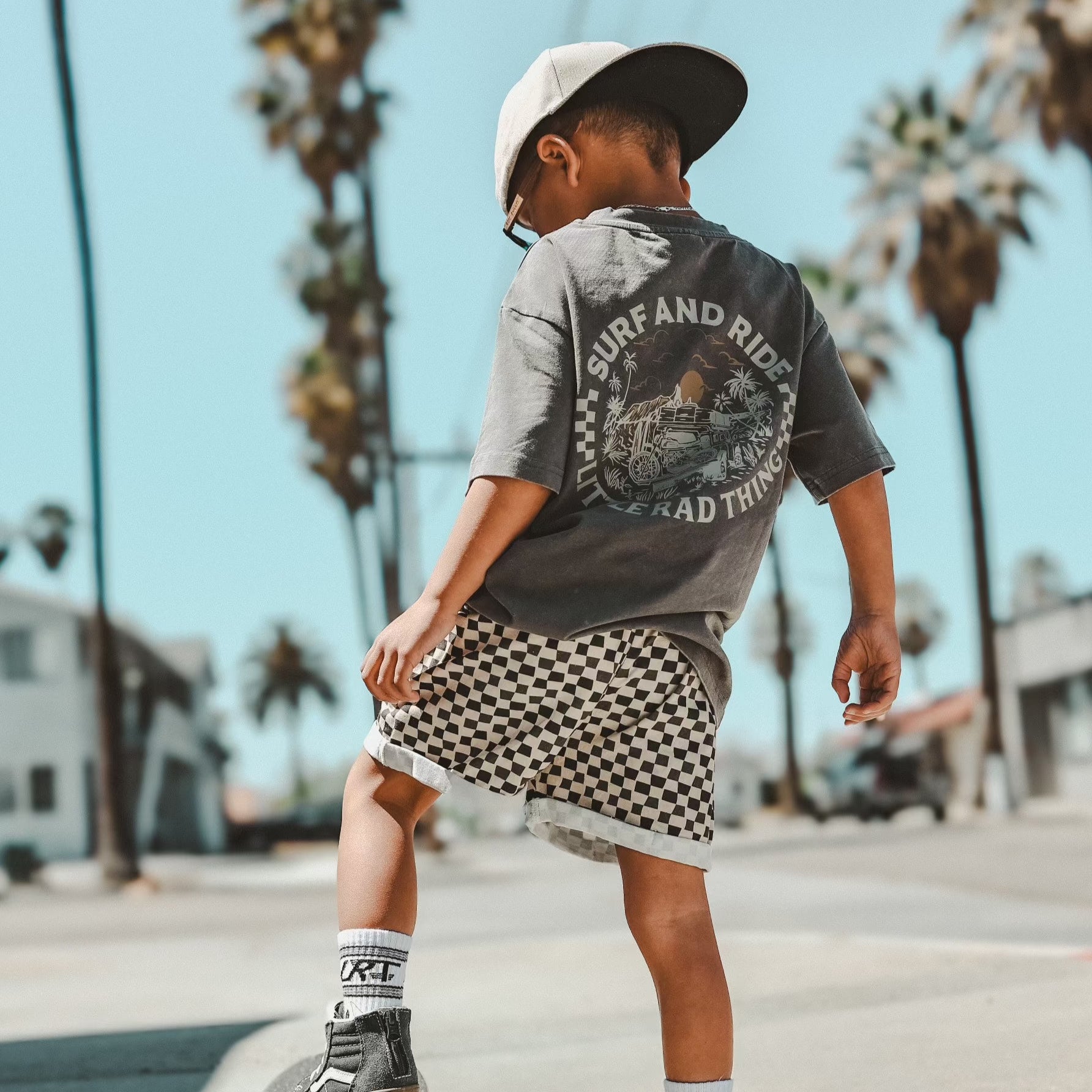 Toddler boy wearing checkerboard shorts and grey t-shirt outdoors.