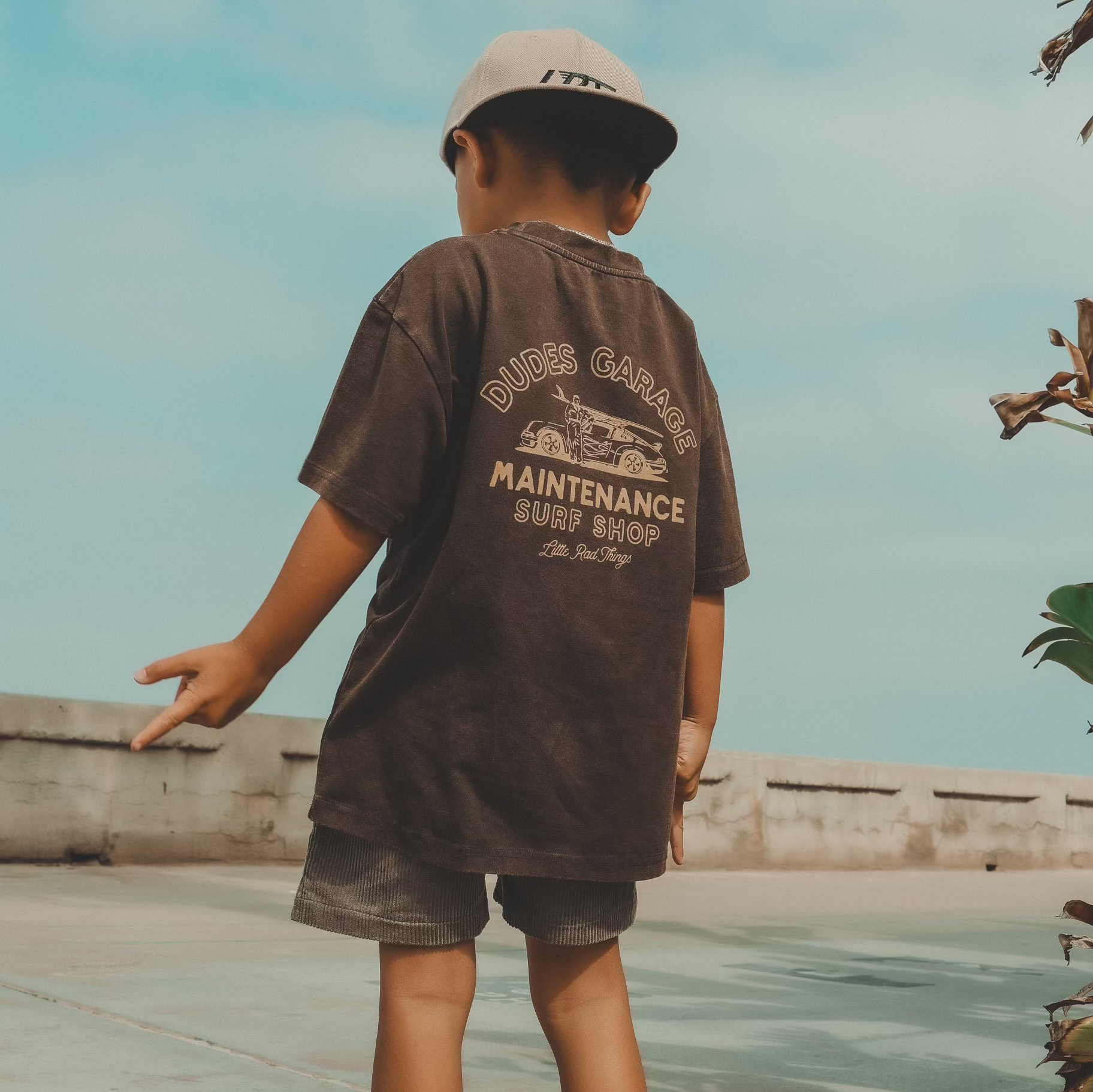 Dudes Garage vintage brown tee featuring surf shop graphic on boy outdoors.