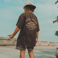 Dudes Garage vintage brown tee featuring surf shop graphic on boy outdoors.