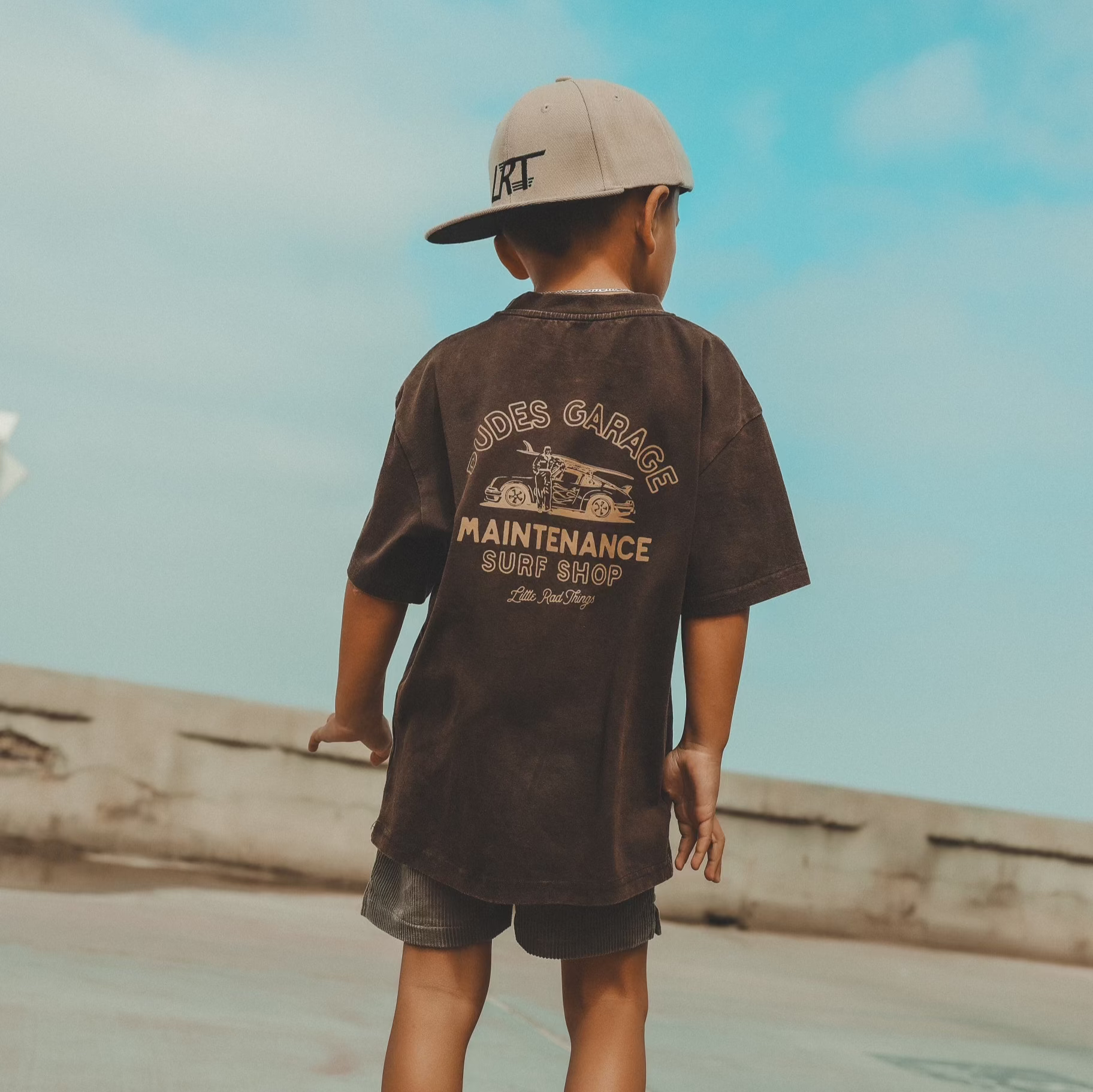 Dudes Garage vintage brown tee featuring surf shop graphic on boy outdoors.