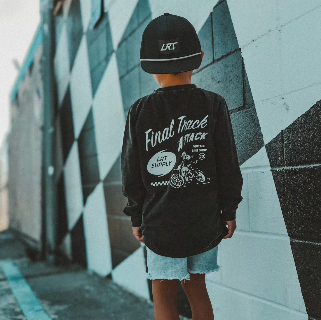 Boy wearing Ocean Cubs Final Track Attack long sleeve tee by checkered wall