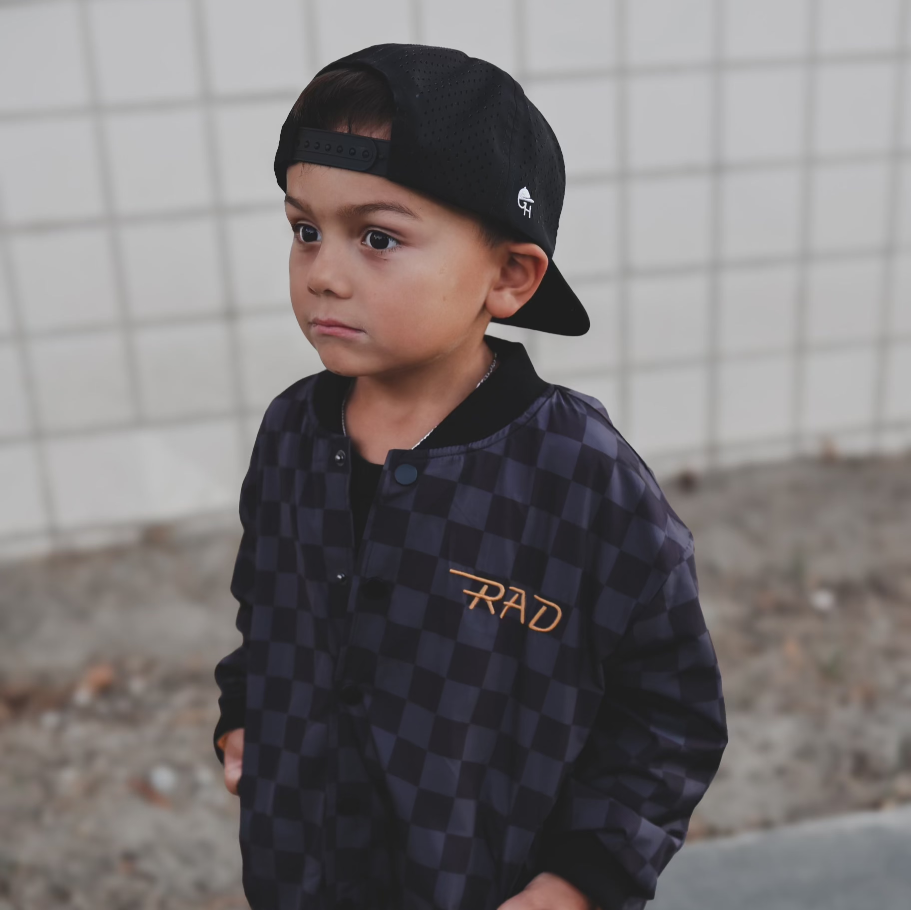 Child wearing a checkered letterman jacket and black baseball cap