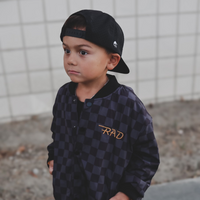 Child wearing a checkered letterman jacket and black baseball cap