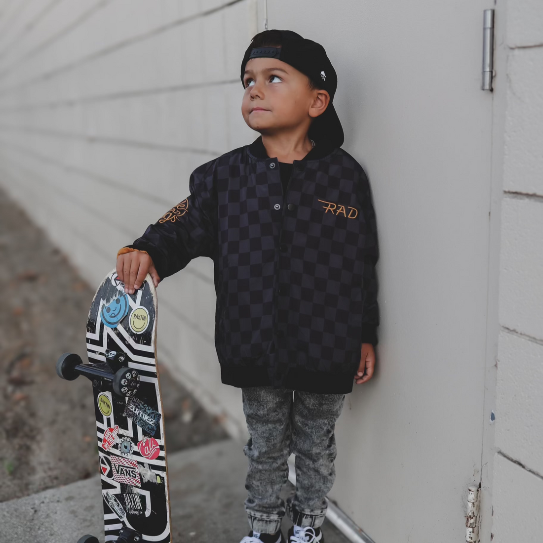 Boy in checkered waterproof letterman jacket with skateboard