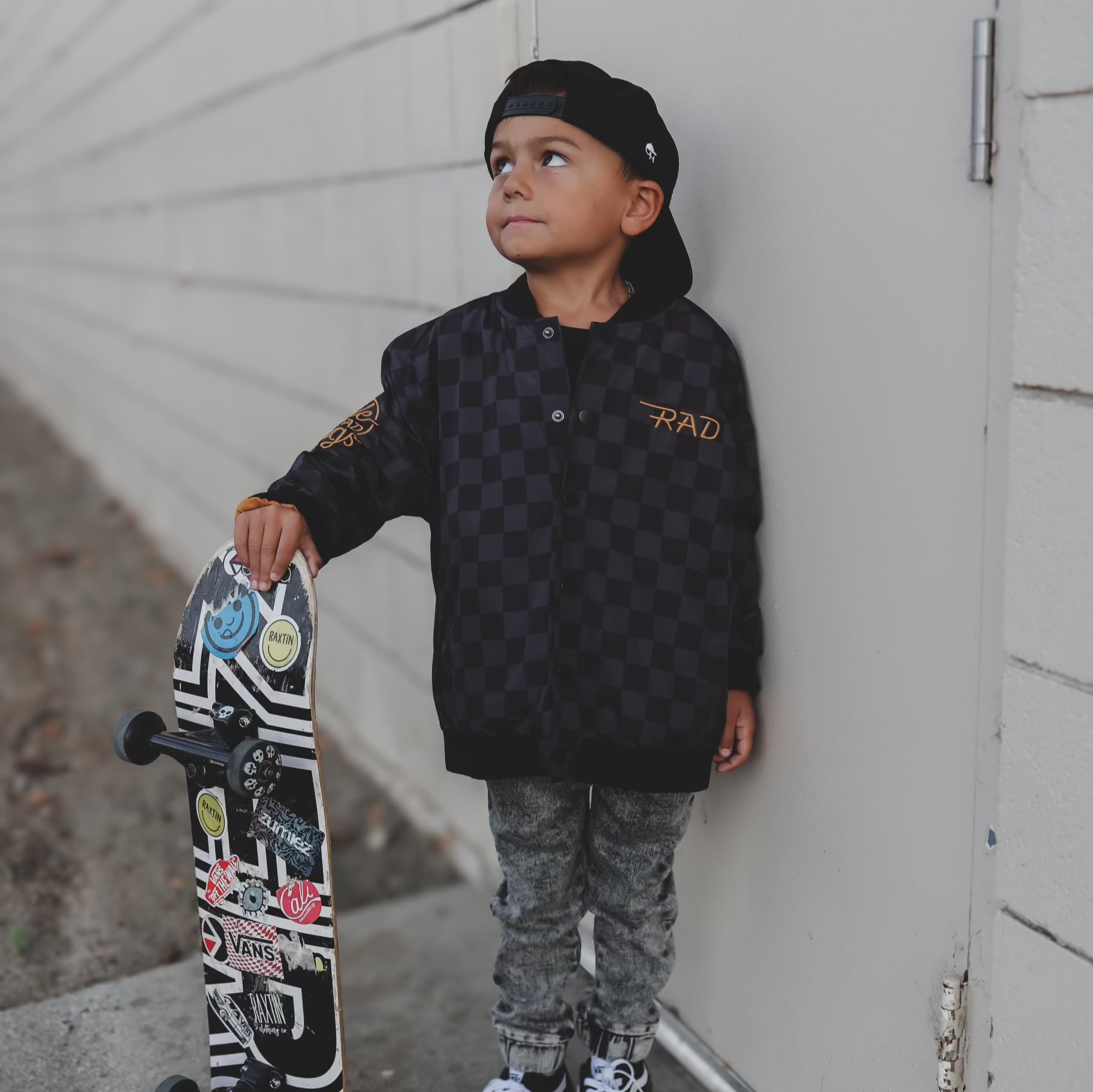 Boy in checkered waterproof letterman jacket with skateboard