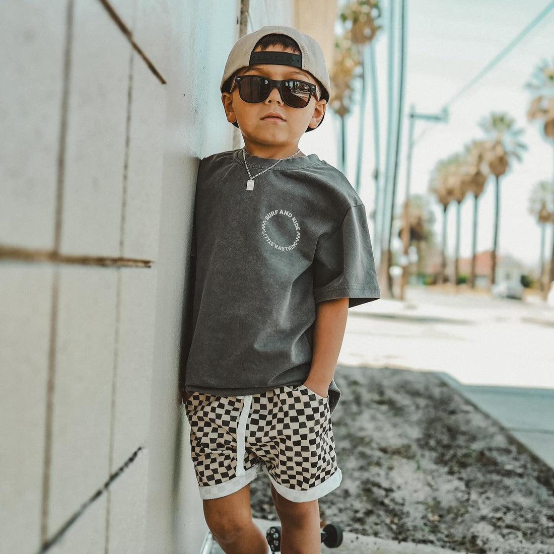 Toddler boy in brown beige checkerboard shorts with t-shirt and sunglasses.