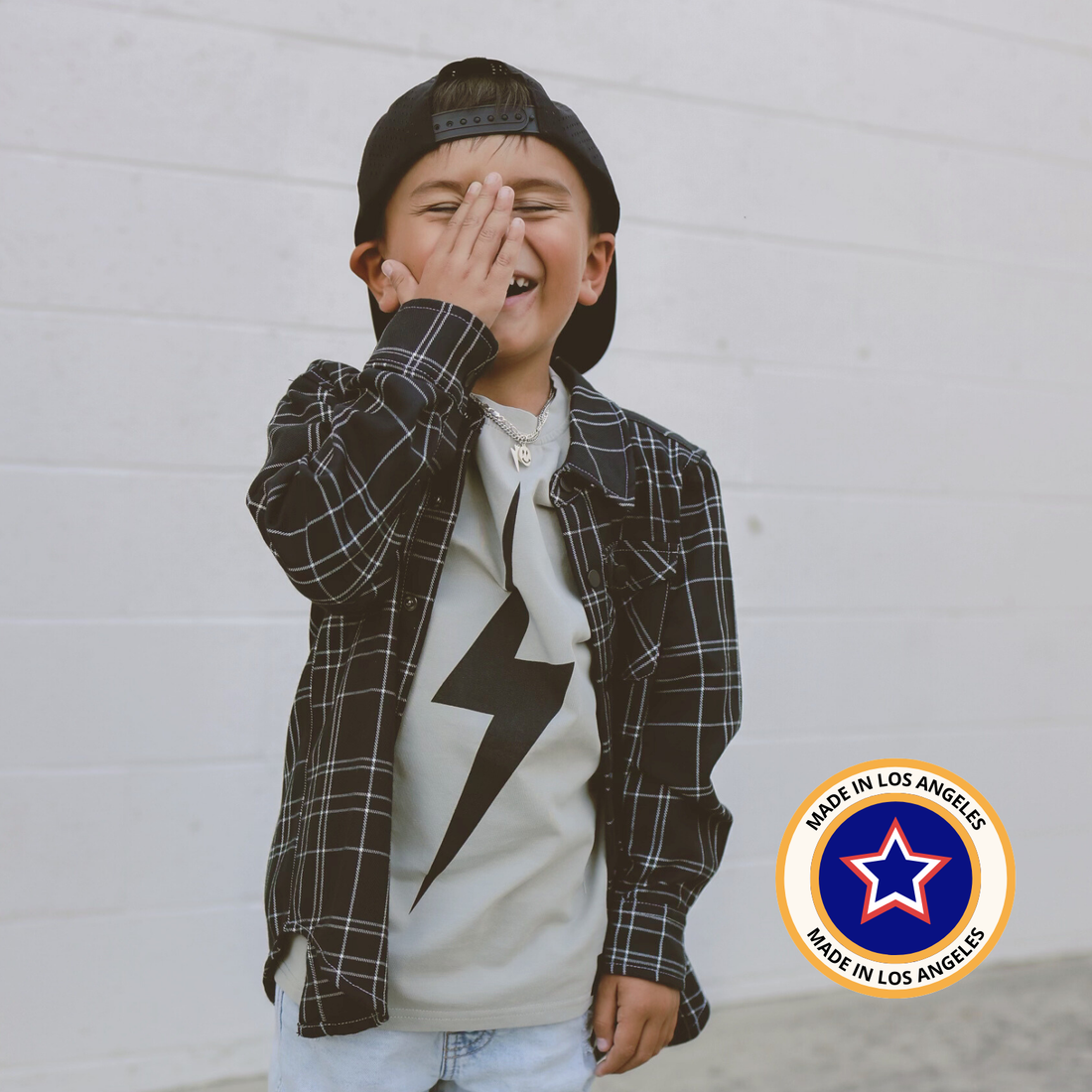 Boy in greige acid wash Spark Tee, black plaid shirt and cap, smiling