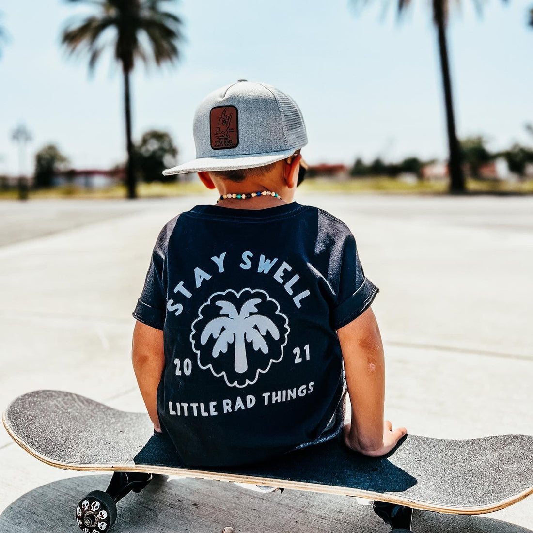 Boy in Stay Swell tee sitting on skateboard outdoors