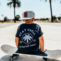 Boy in Stay Swell tee sitting on skateboard outdoors