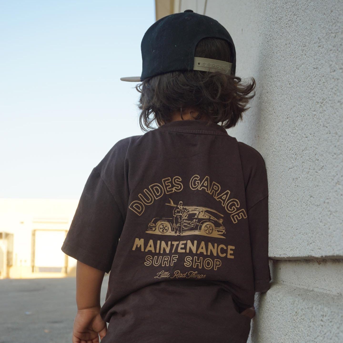 Dudes Garage vintage brown tee featuring surf shop graphic on boy outdoors.