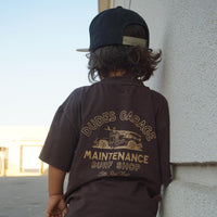 Dudes Garage vintage brown tee featuring surf shop graphic on boy outdoors.