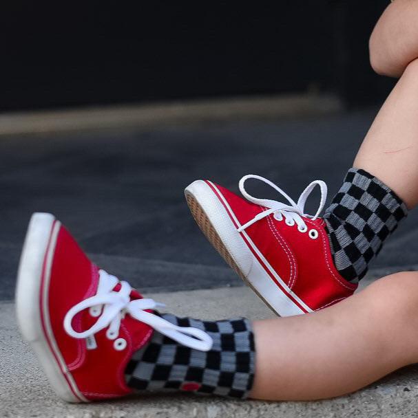 Toddler wearing checkered Check The Volts socks with red Vans sneakers.
