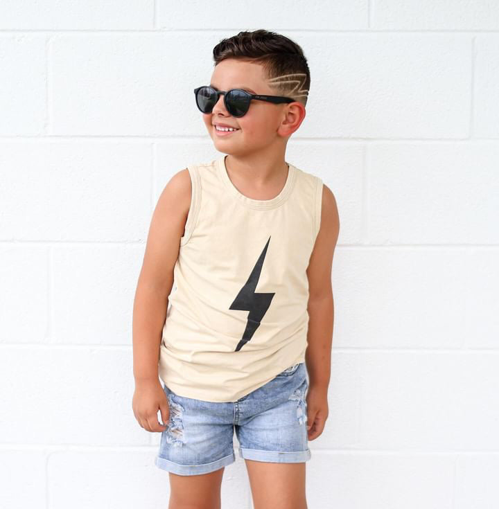 Boy in greige Spark Muscle Tee and denim shorts smiles in sunglasses