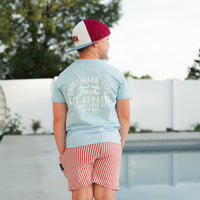 Boy wearing cloud blue APEX LIVE FAST tee, back view, by the pool.