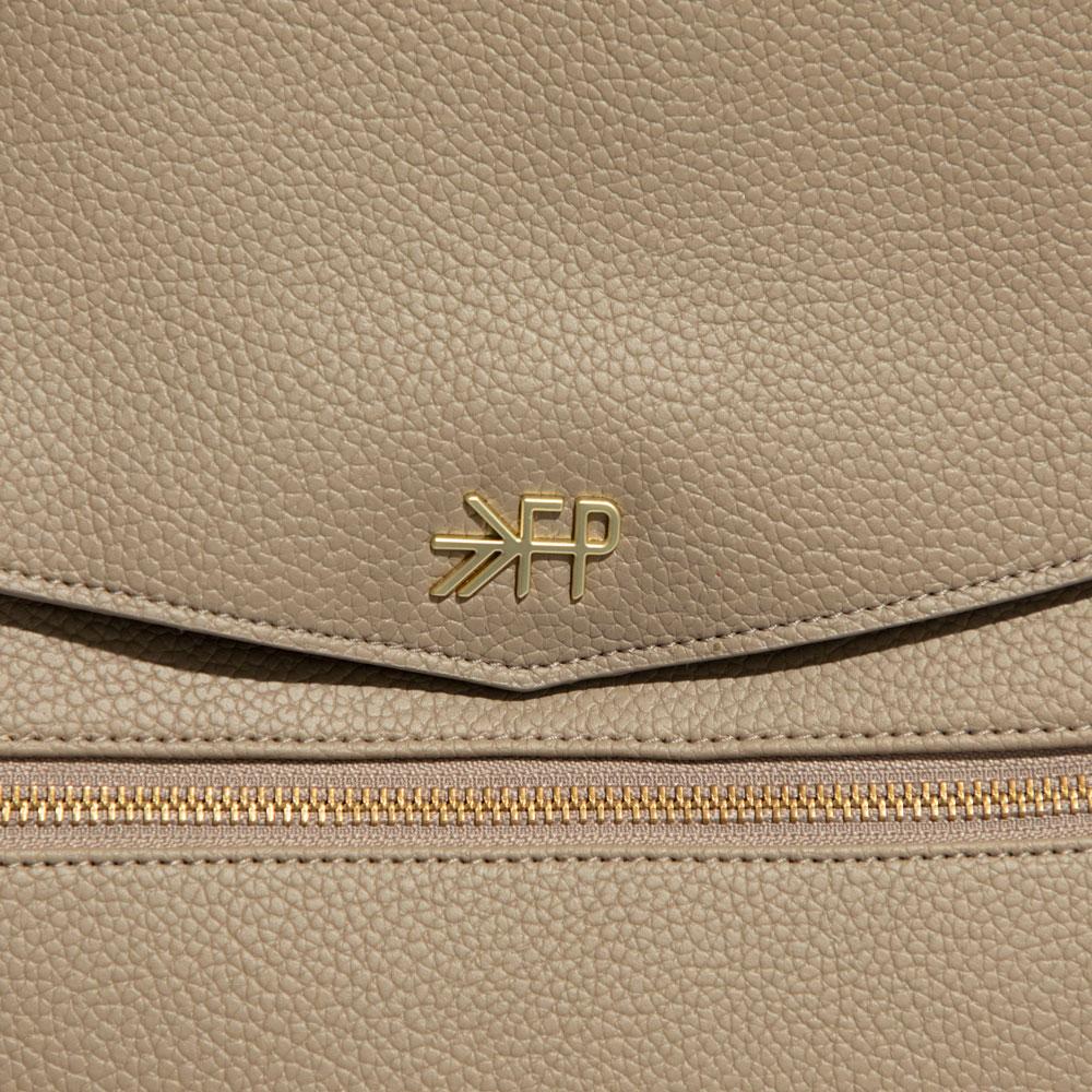Close-up of the Aspen Diaper Bag II in stone, showing the logo and zipper detail.