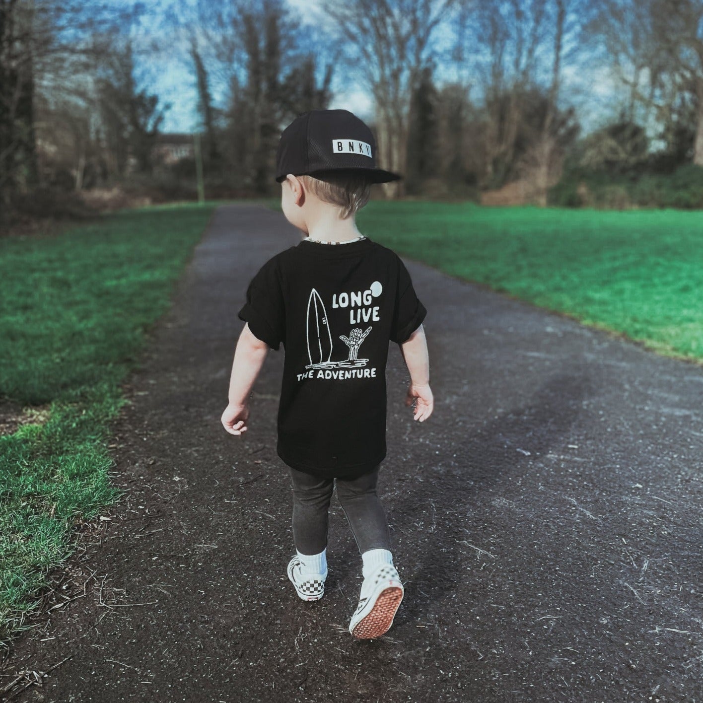 Boy in Long Live The Adventure black tee walking on path.