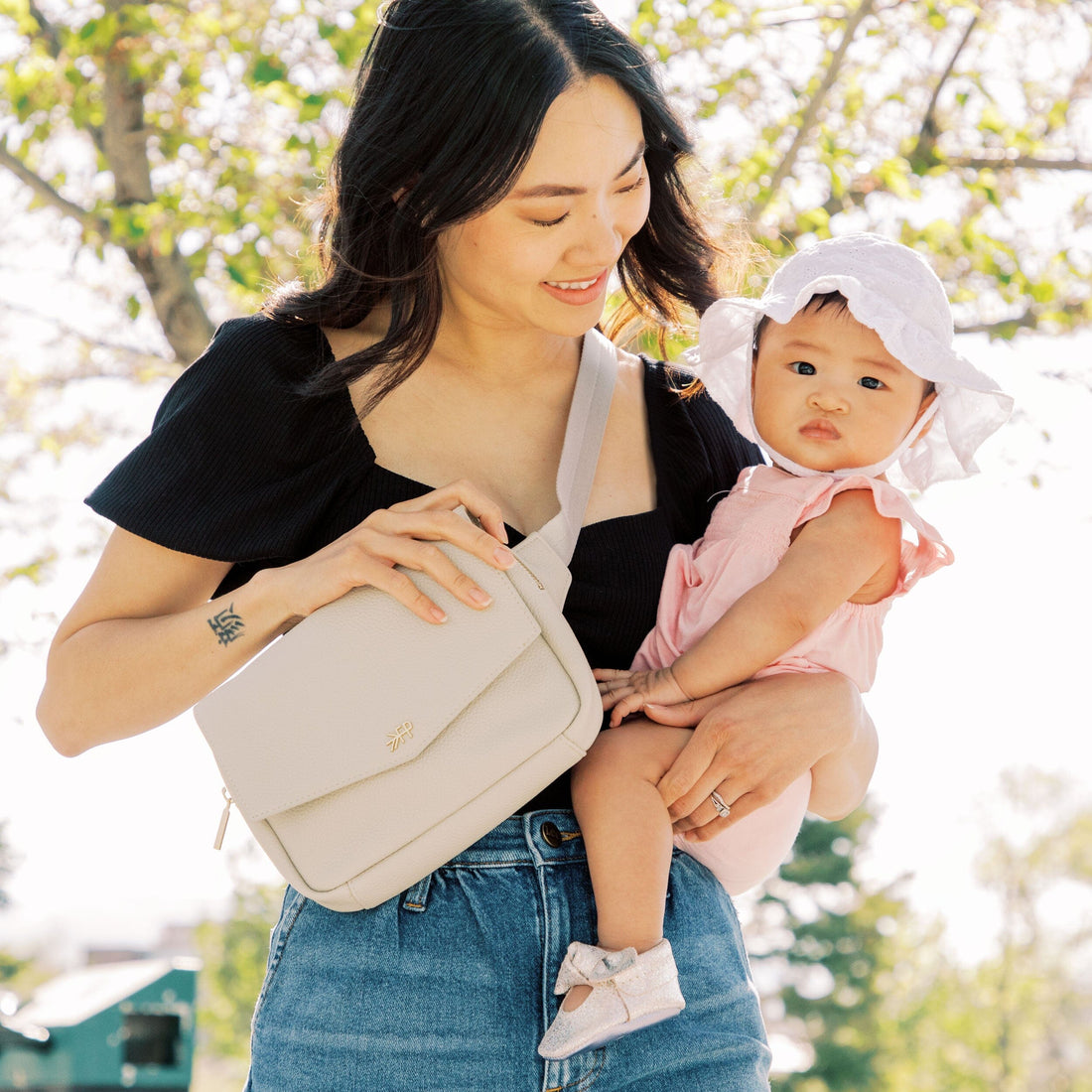 Mom holding baby, wearing Birch Classic Park Pack as crossbody bag