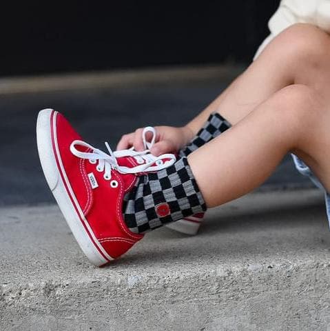 Toddler wearing checkered Check The Volts socks with red Vans sneakers.