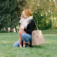 A parent hugs their child while wearing the Aspen Diaper Bag II in stone.