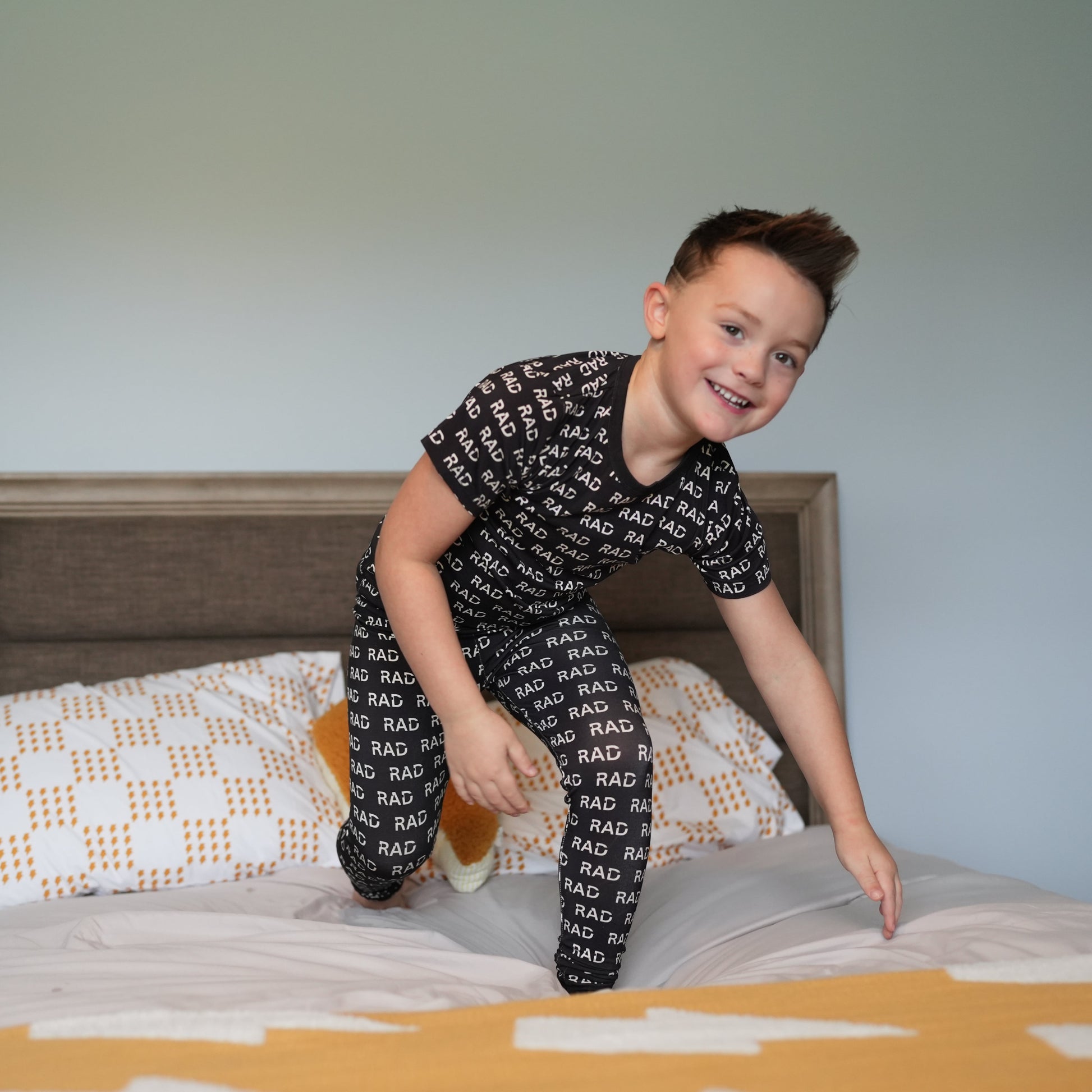 Boy in black RAD print pajamas jumping on the bed.
