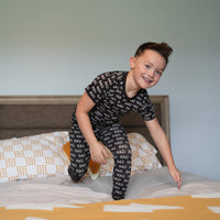 Boy in black RAD print pajamas jumping on the bed.