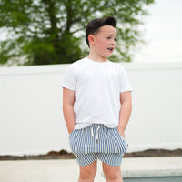 Boy posing in RAD Organics white tee and striped swim trunks.