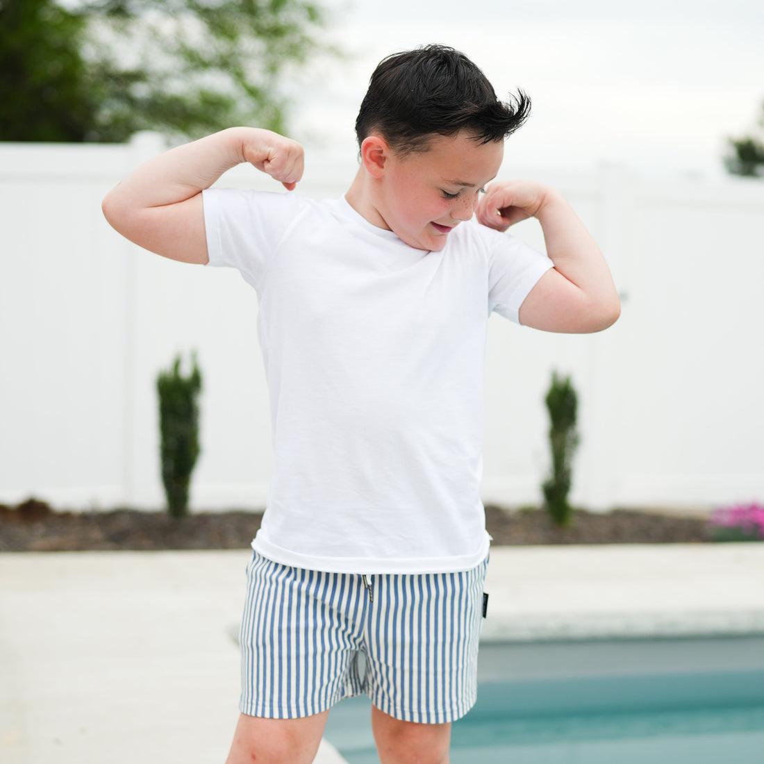 Boy flexing in RAD Organics white tee and striped swim trunks.