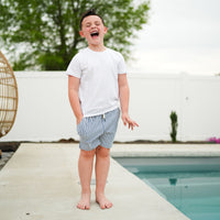Boy laughing by pool in RAD Organics white tee and striped swim trunks.
