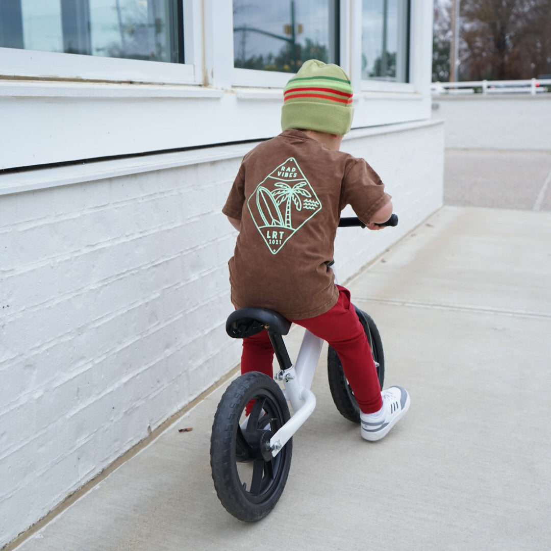 Child on bike wearing Cocoa Beach Tee with retro surf design.