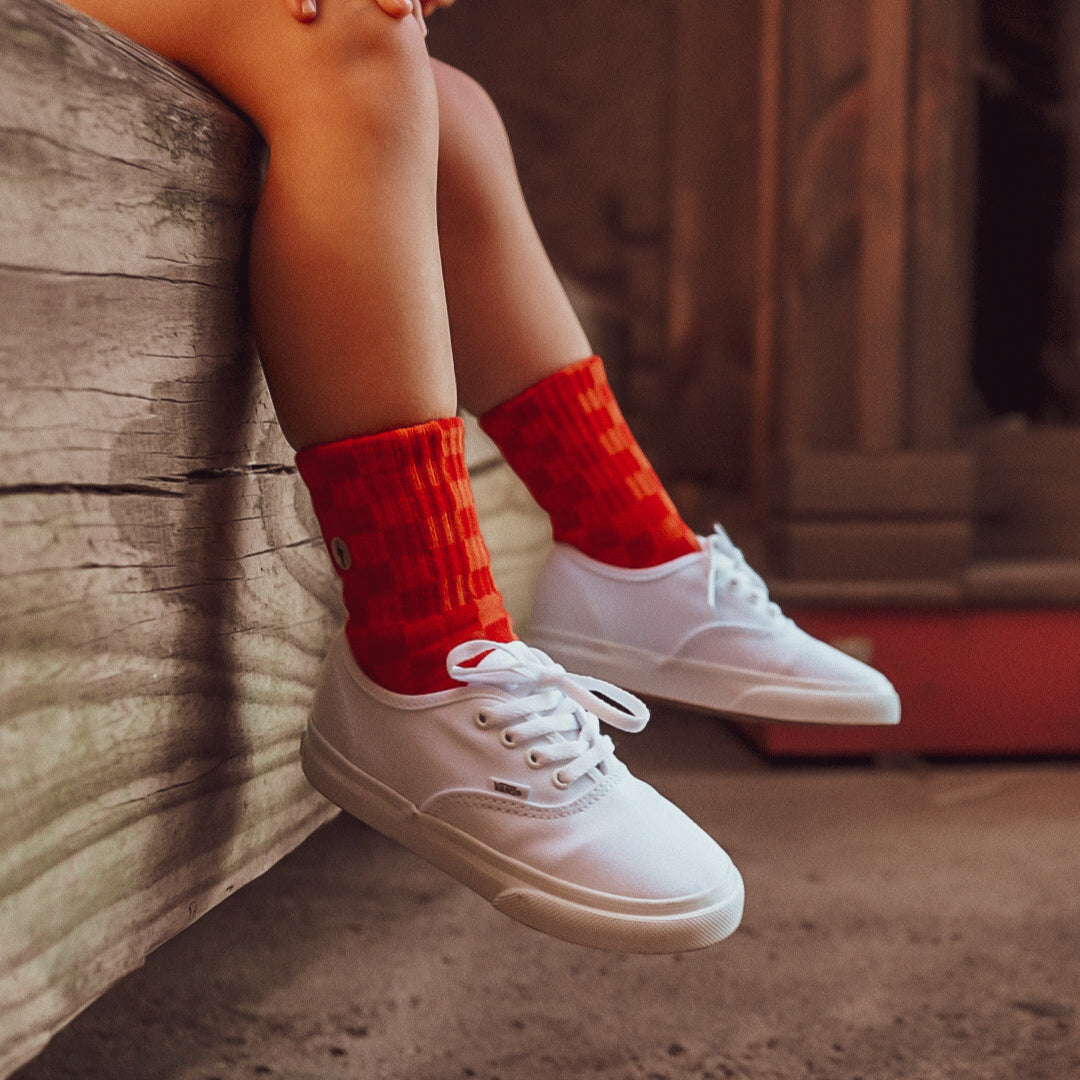 Child wearing Retrograde red/orange checkered socks with white sneakers.