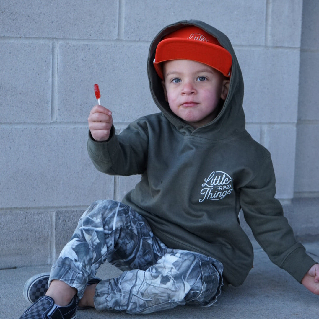 Boy in army green Radiator Hoodie with orange hat and lollipop.
