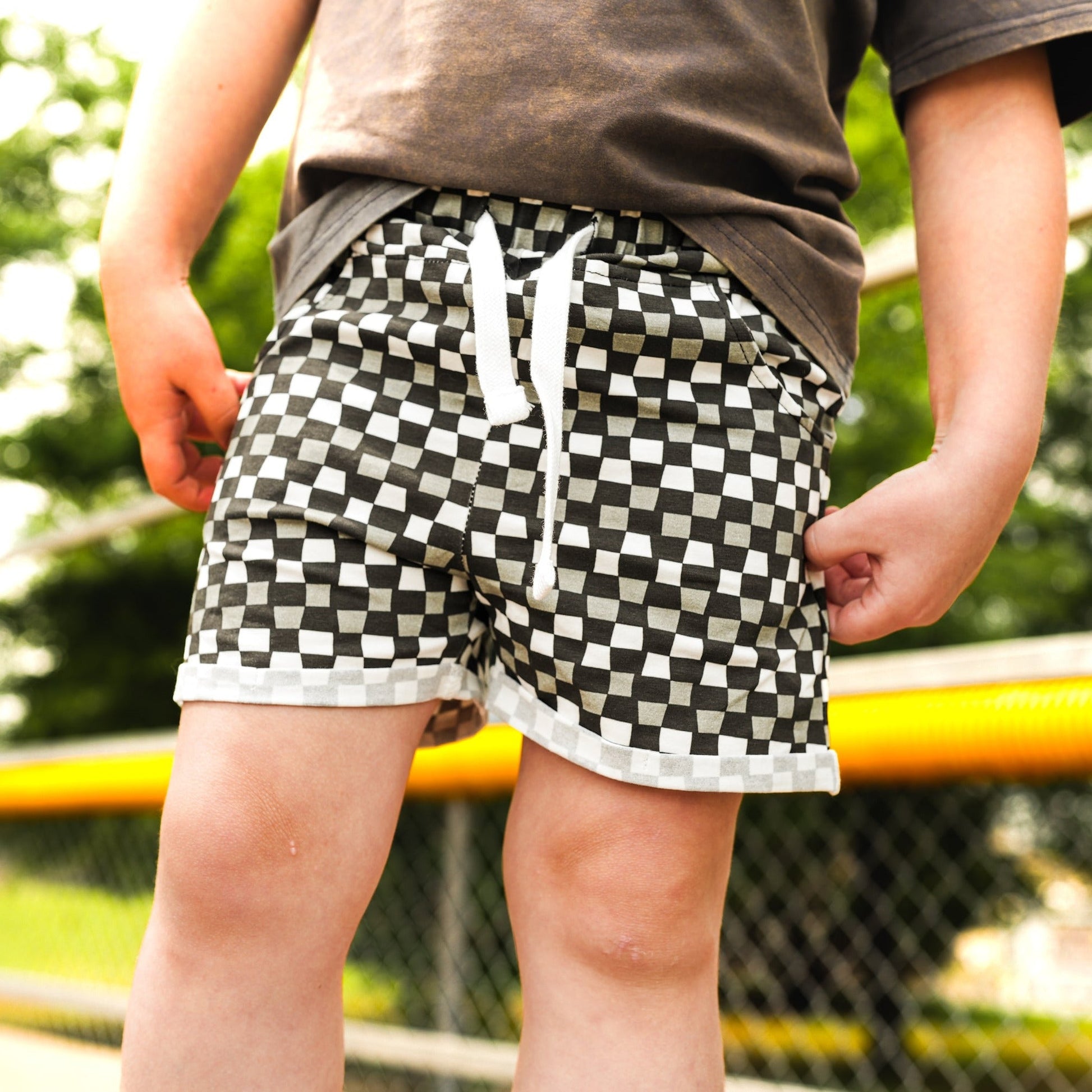 Boy wearing 'Check Ya Later' shorts in black, grey, and white check pattern.