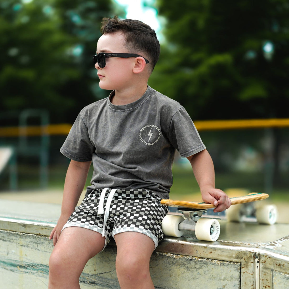 Boy in sunglasses wearing black and grey checkered 'Check Ya Later' shorts.