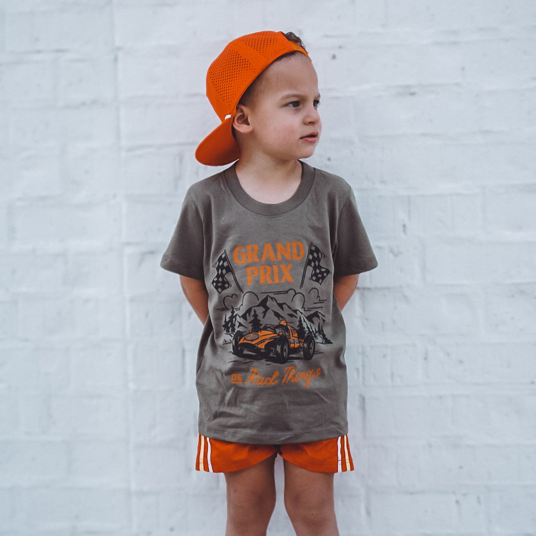 Boy in military green Grand Prix tee, orange cap and shorts.