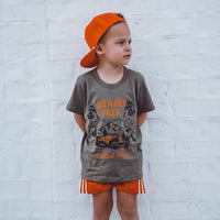 Boy in military green Grand Prix tee, orange cap and shorts.