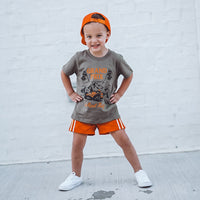 Child wearing military green Grand Prix tee playing outside.