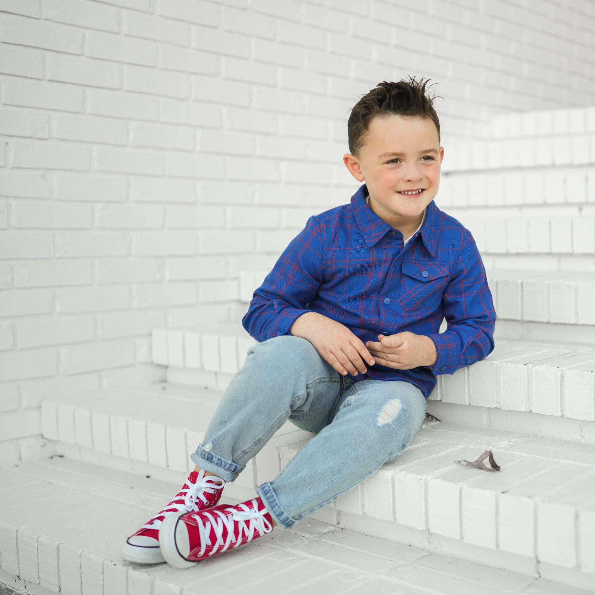 Smiling boy in blue plaid Kids Fast and Free Flannel on white steps