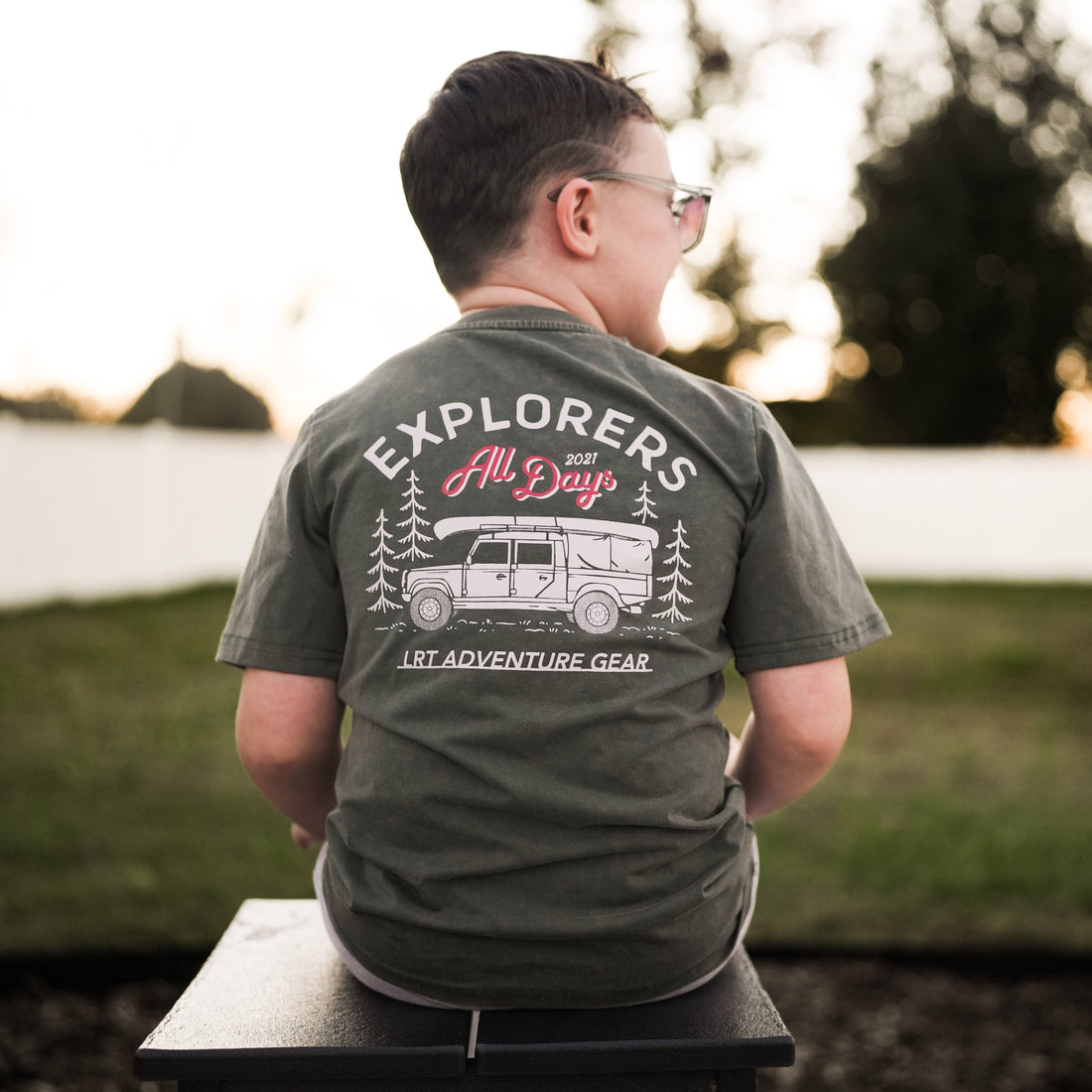 Boy wearing sage green Explorer tee with truck graphic on back.