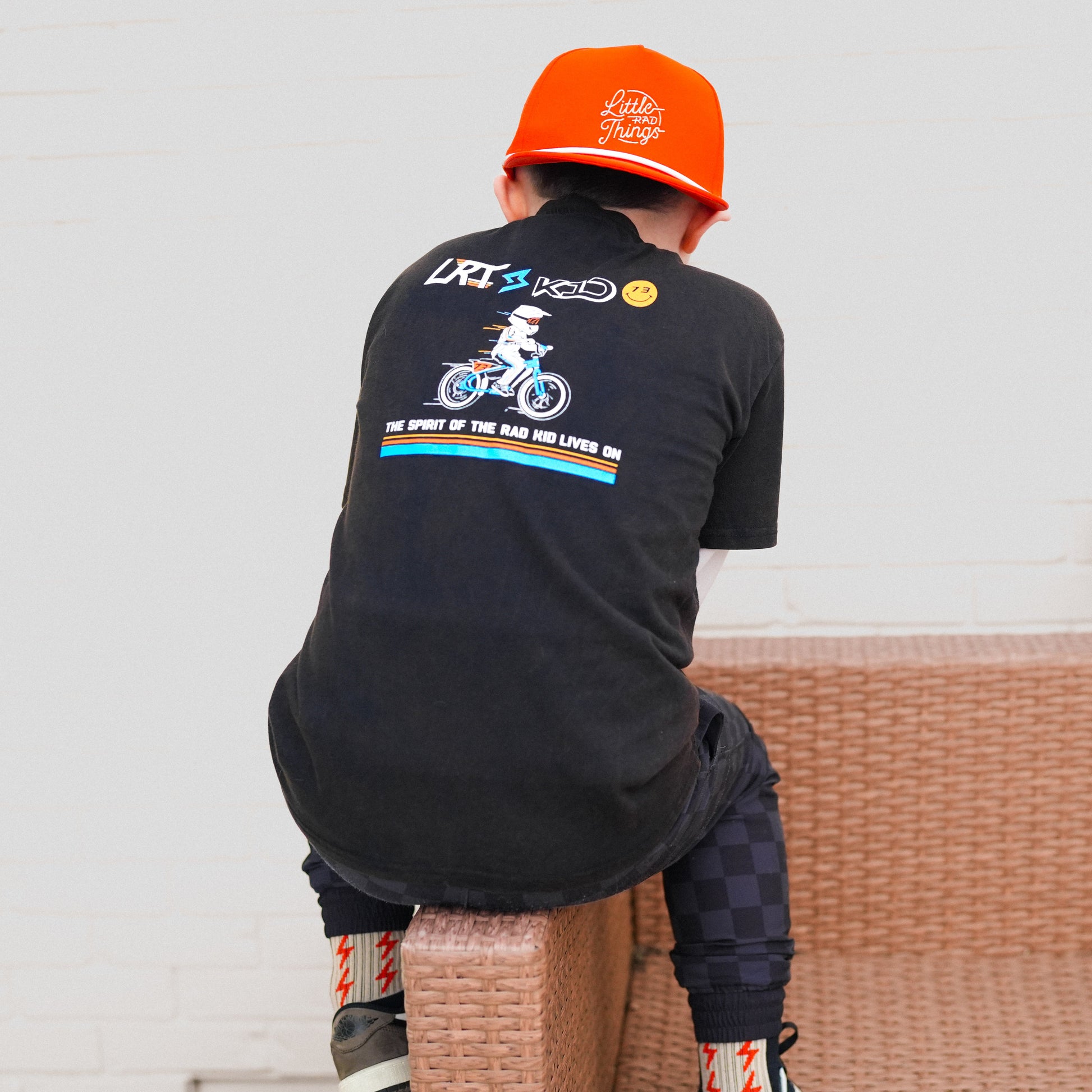 Child wearing LRT x SUPER73 black collab tee sitting, back view of tee graphic.