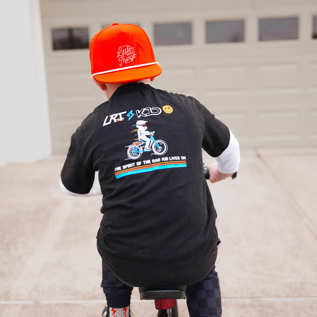 LRT x SUPER73 collab tee on child riding bike, back view, showing graphic print.