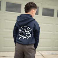 Child in navy Radiator Hoodie with 'Little Rad Things' design, standing in front of a garage.