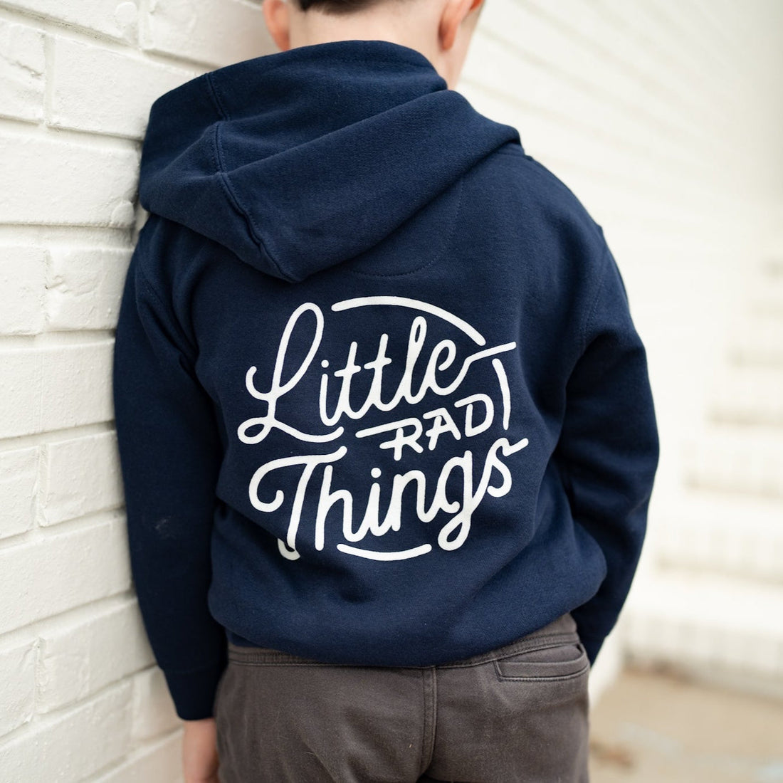 Back view of a child wearing a navy Radiator Hoodie with 'Little Rad Things' design.